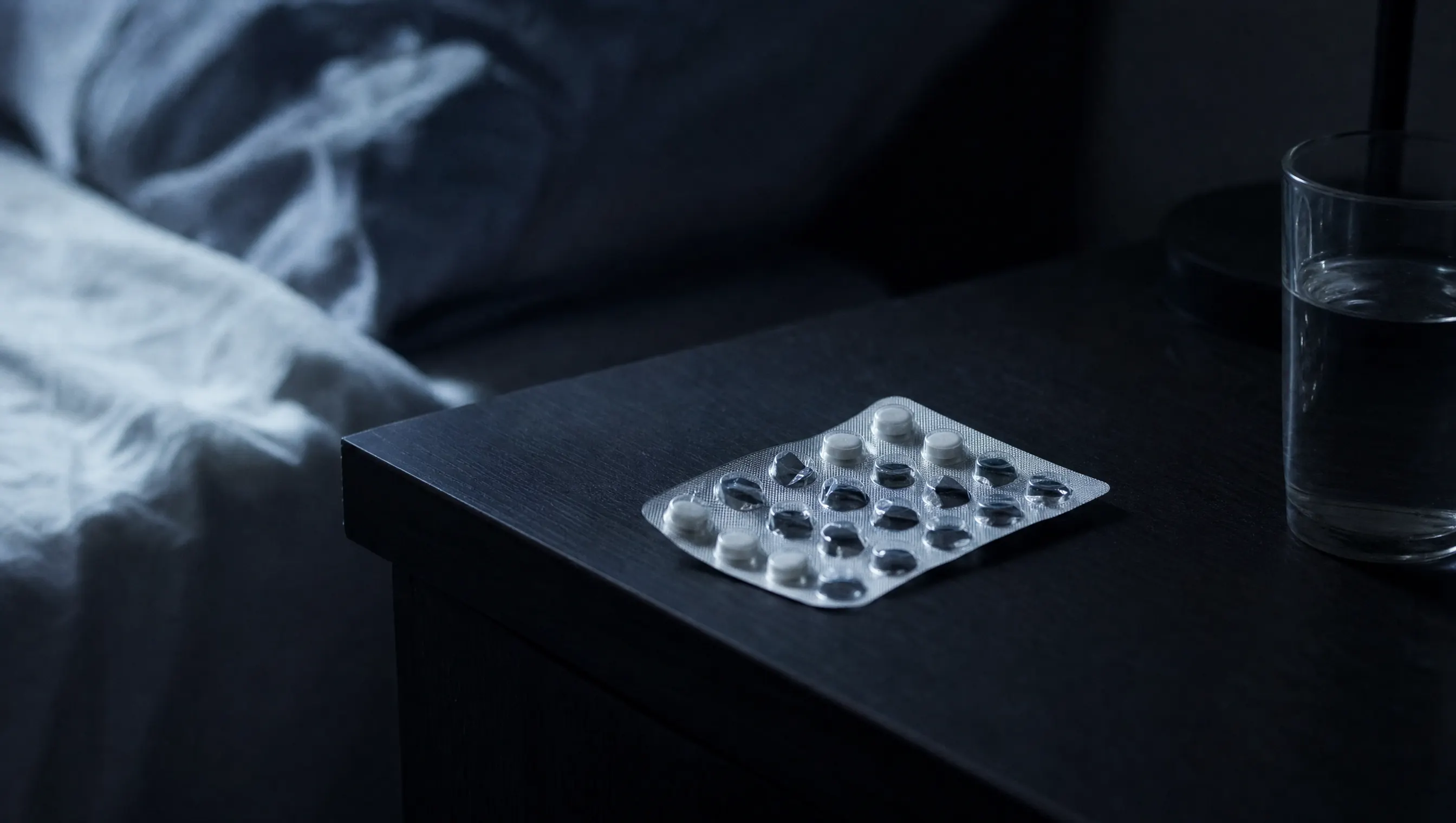 Caja genérica de pastillas sin marca sobre una mesa de noche con luz fría de madrugada