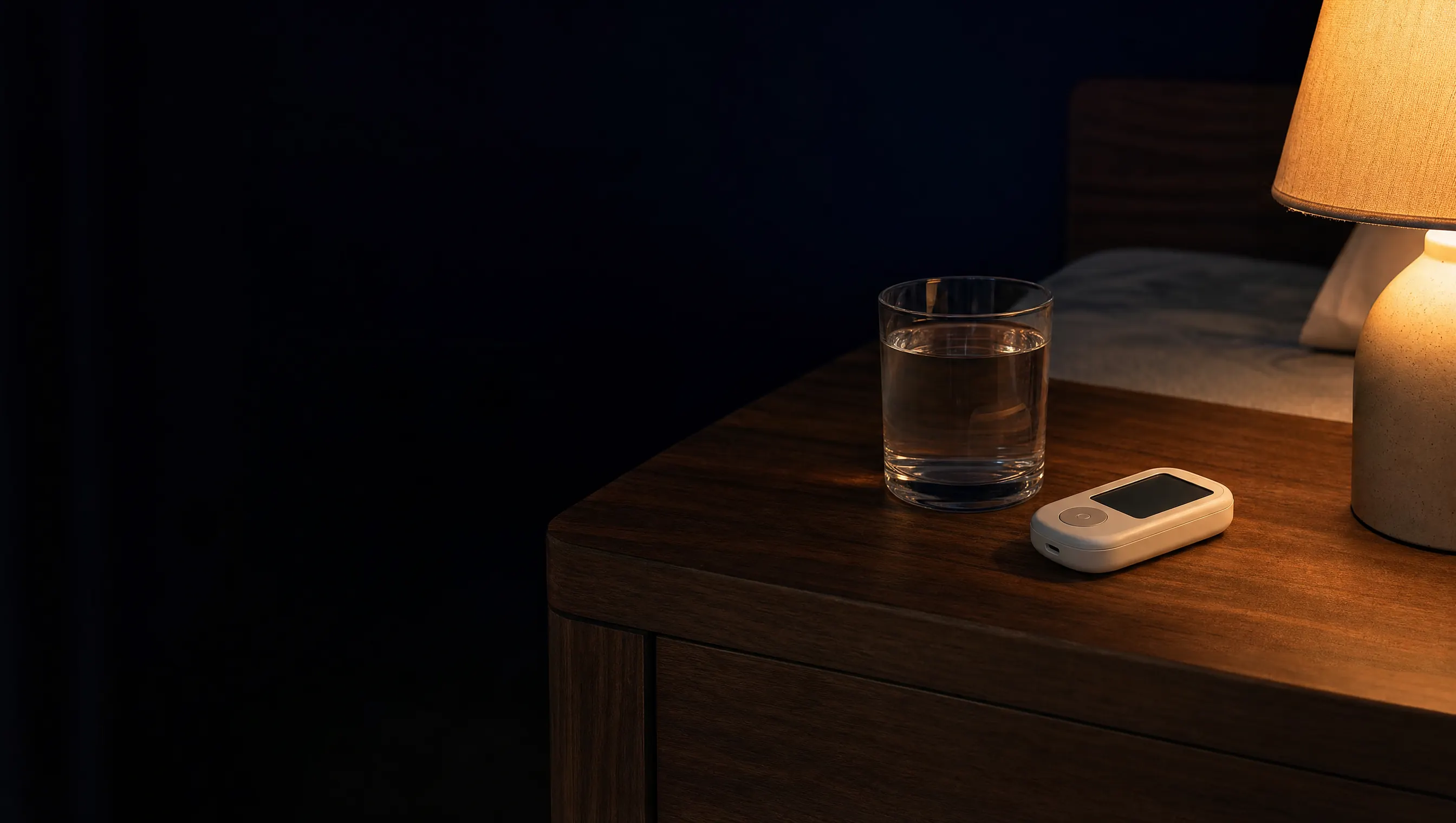 Vaso de agua y un glucómetro sobre una mesa de noche en penumbra