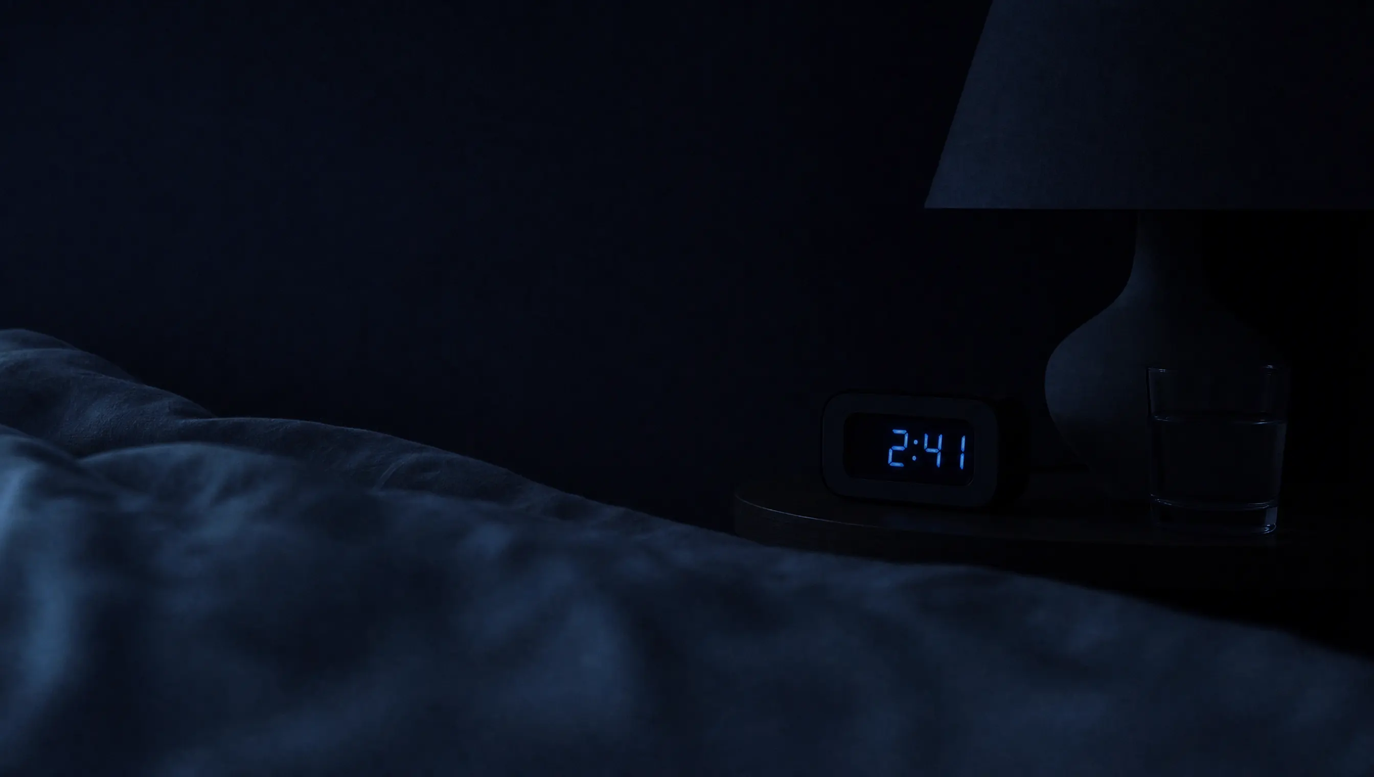 Habitación a oscuras con una cama deshecha y la luz azulada de un reloj marcando la madrugada