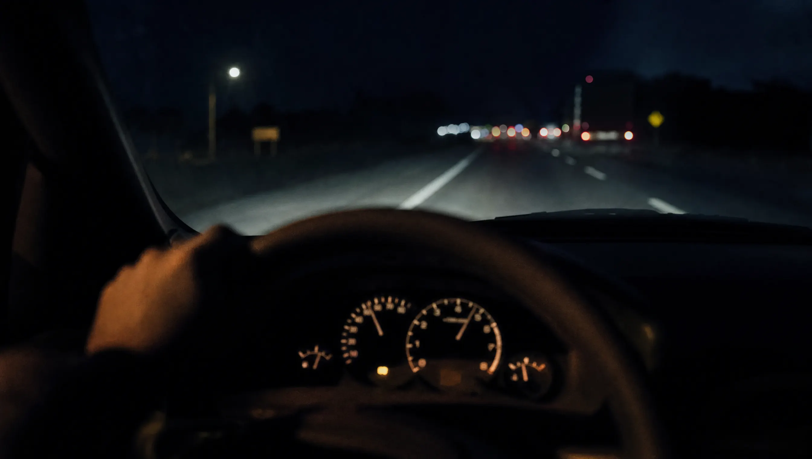 Carretera nocturna vista desde el asiento del conductor, con las luces del tablero y la vía difuminada al frente