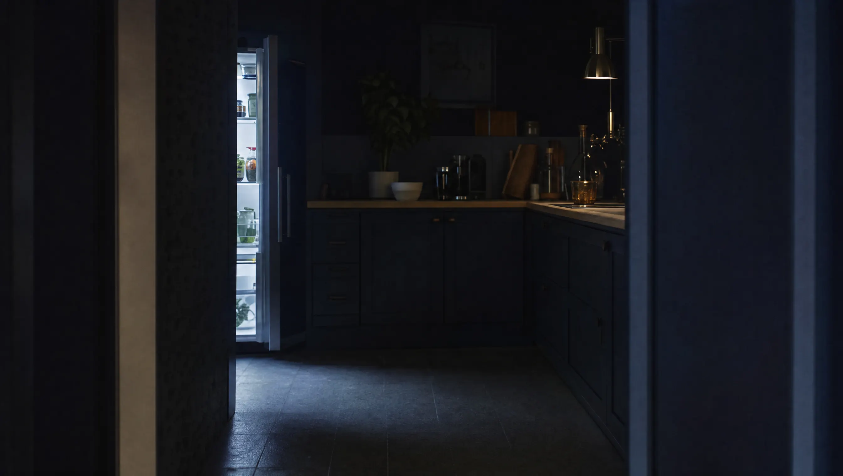 Cocina en penumbra de madrugada con la puerta de la nevera entreabierta proyectando luz fría